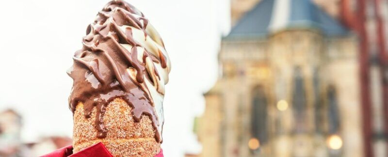 La main d'une femme tient un biscuit traditionnel tchèque, le trdelnik, sur fond de vieille ville de Prague. Meilleures Glaceries à Paris